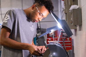 NWTC CNC Machinist Student Reyniel Folwarski works at a grinder in the Gene Haas Center for Advanced Machining. 