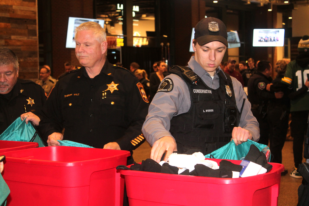 Wisconsin DNR Conservation Warden Logan Woods, on right, packs a backpack with essentials during the Police Lights of Love event in the Johnsonville Tailgate Village at Lambeau Field on Nov. 27. Kris Leonhardt photos